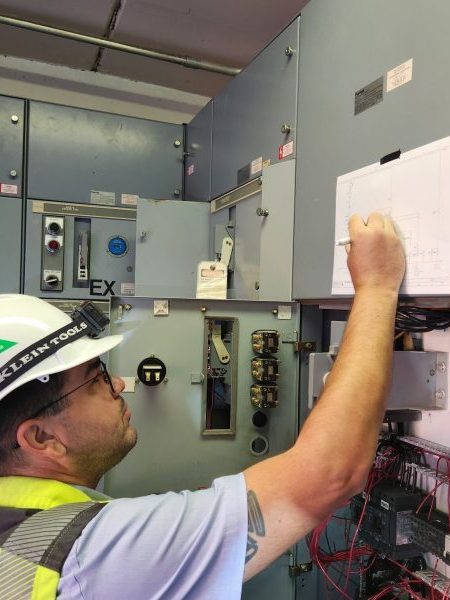 Eletricista conferindo o diagrama elétrico durante manutenção em um cubículo de manobra